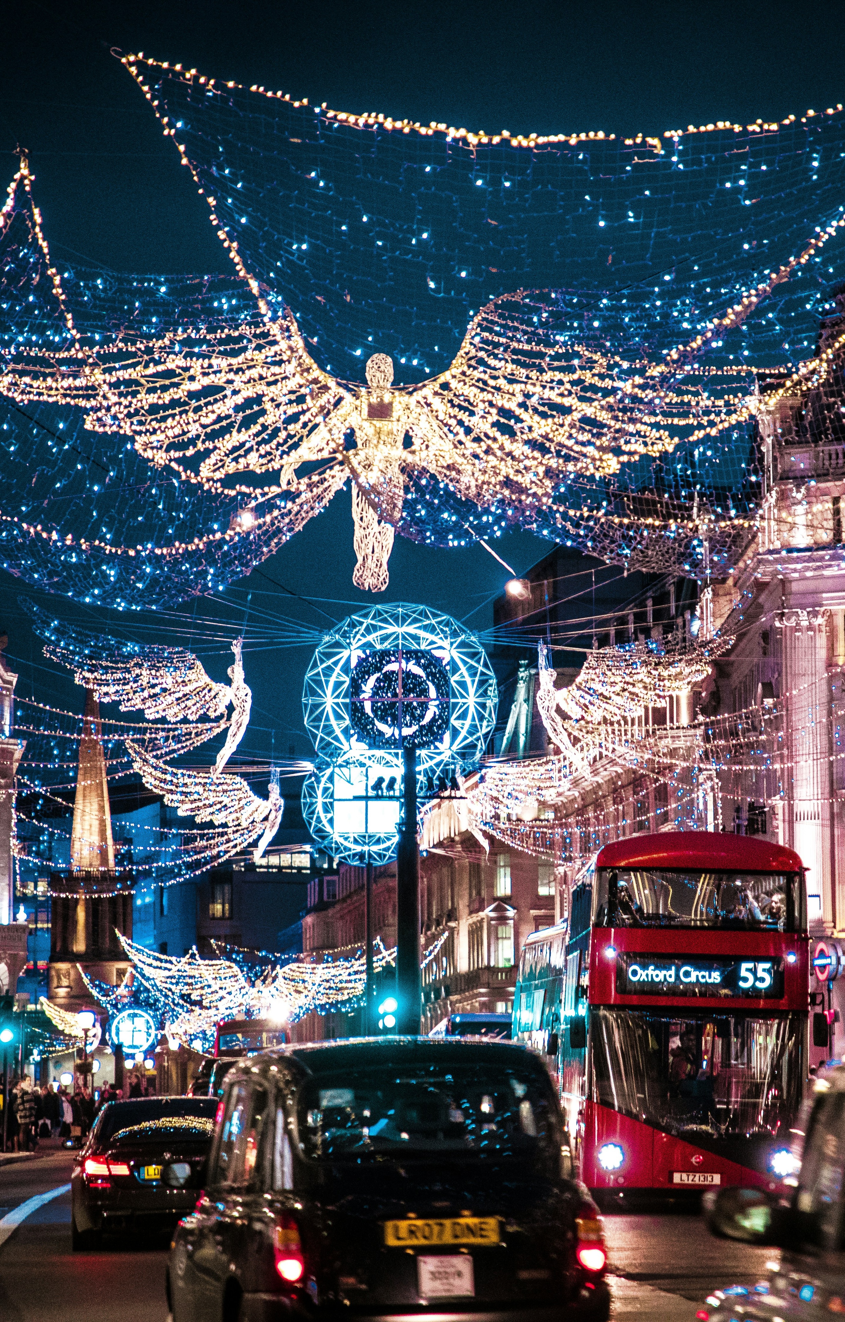Festive Christmas lights shaped like angels above Regent Street in London, with a red double-decker bus and busy evening traffic.