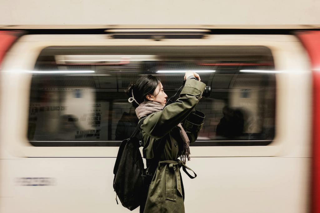 A tourist taking a photo of the iconic London Underground sign at a bustling Tube station