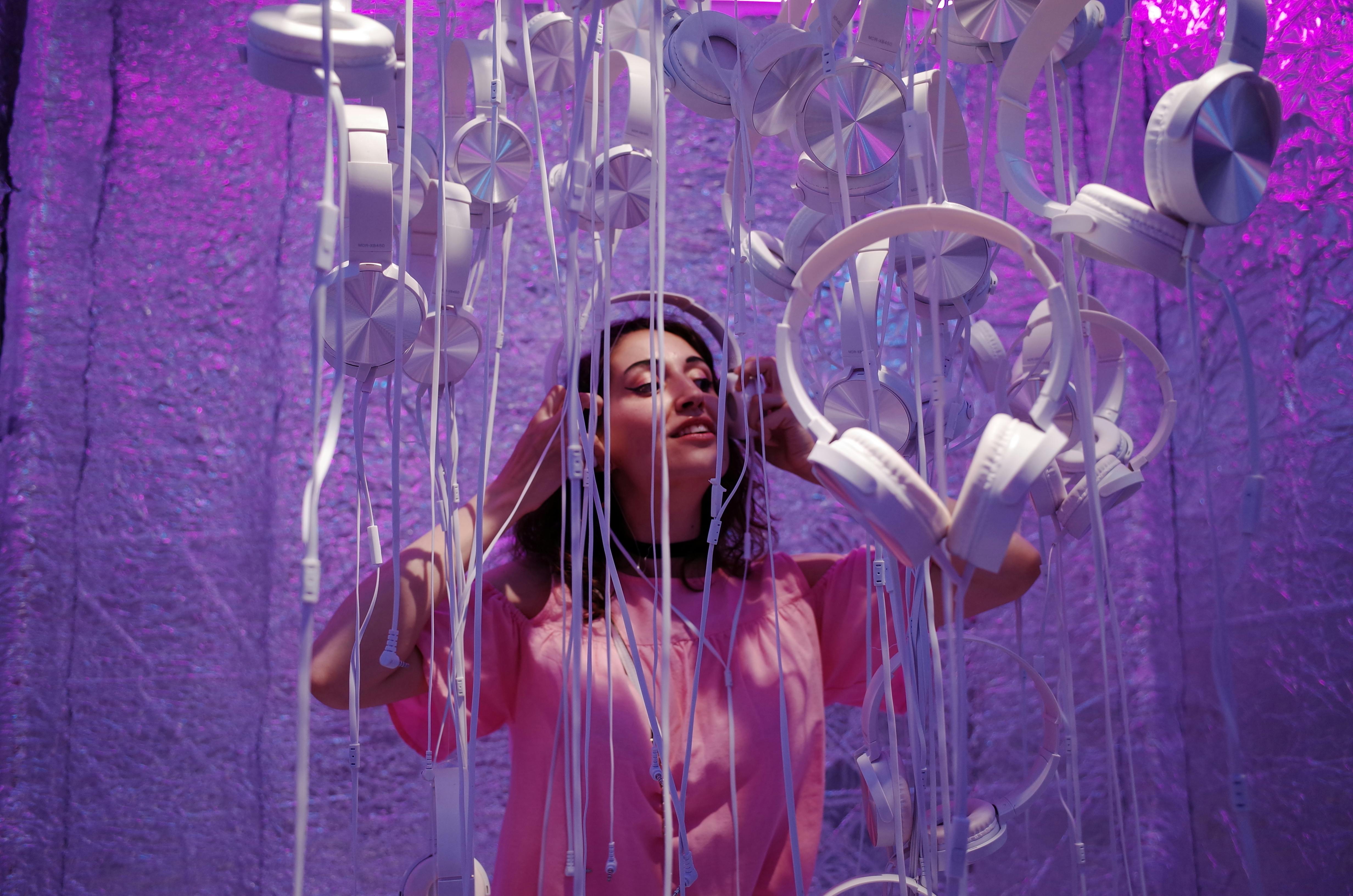 A woman enjoying a unique multi-sensory experience at an immersive exhibit in London, surrounded by hanging headphones and vibrant lighting.