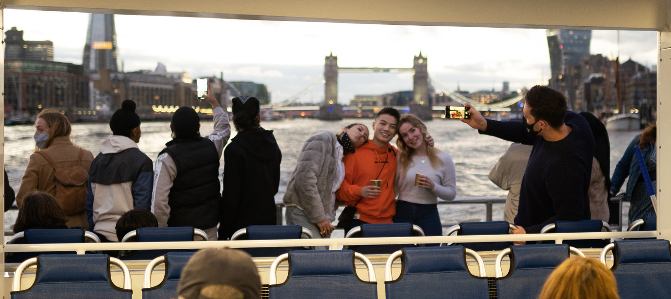 Group of friends and tourists enjoying a boat ride on the River Thames with Tower Bridge in the background, London sightseeing experience